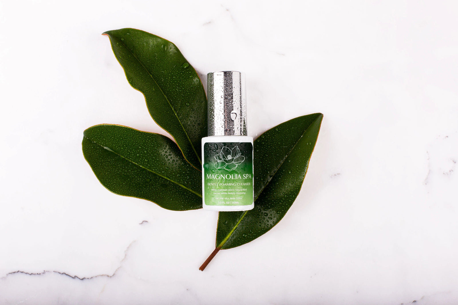 Green gradient cleanser bottle resting on magnolia leaves